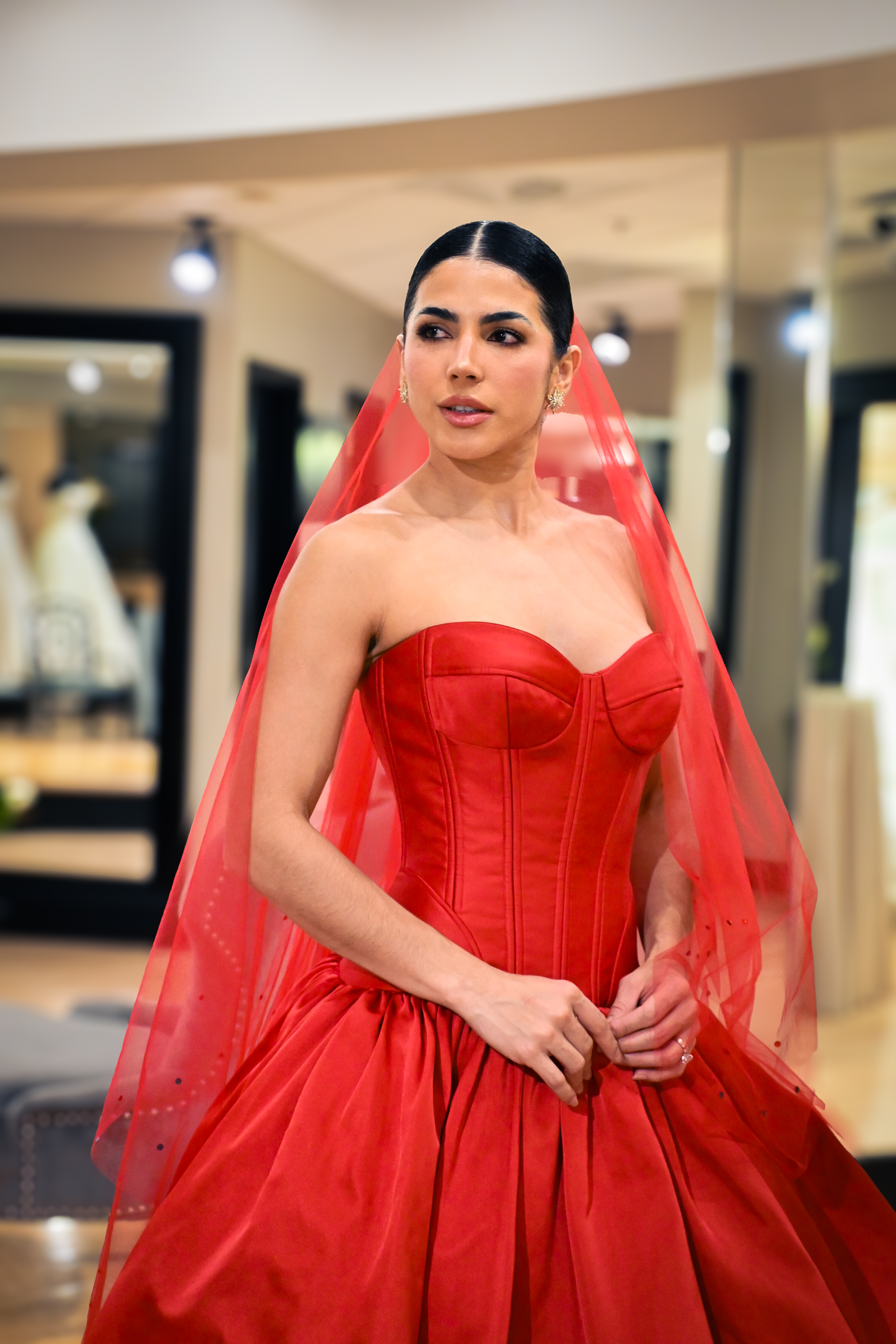Model wearing a dramatic red strapless ball gown with a structured corset bodice and matching sheer red veil, posing inside Bridals by Lori in Atlanta with softly lit mirrors and bridal displays in the background.